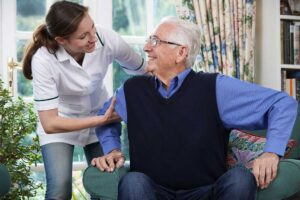 An elderly person using a walker with the support of a caregiver in a bright, accessible hallway.