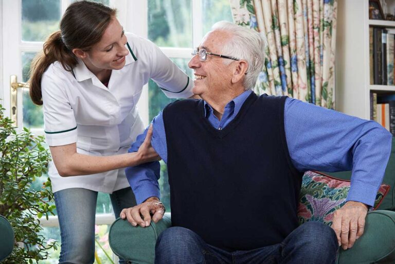 An elderly person using a walker with the support of a caregiver in a bright, accessible hallway.