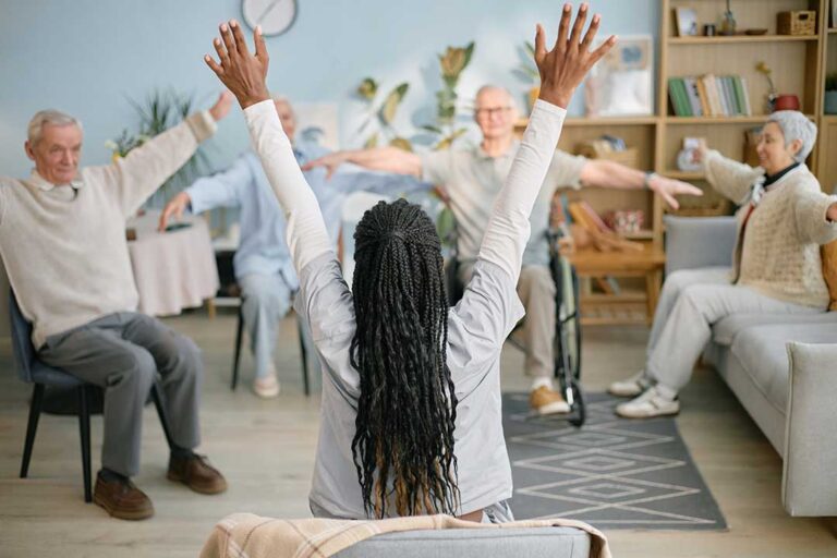 Residents and staff sitting together in a brightly lit common room, smiling and talking comfortably.